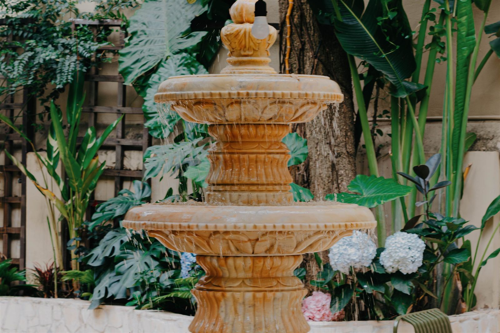 Three-tier stone outdoor garden fountain surrounded by lush greenery